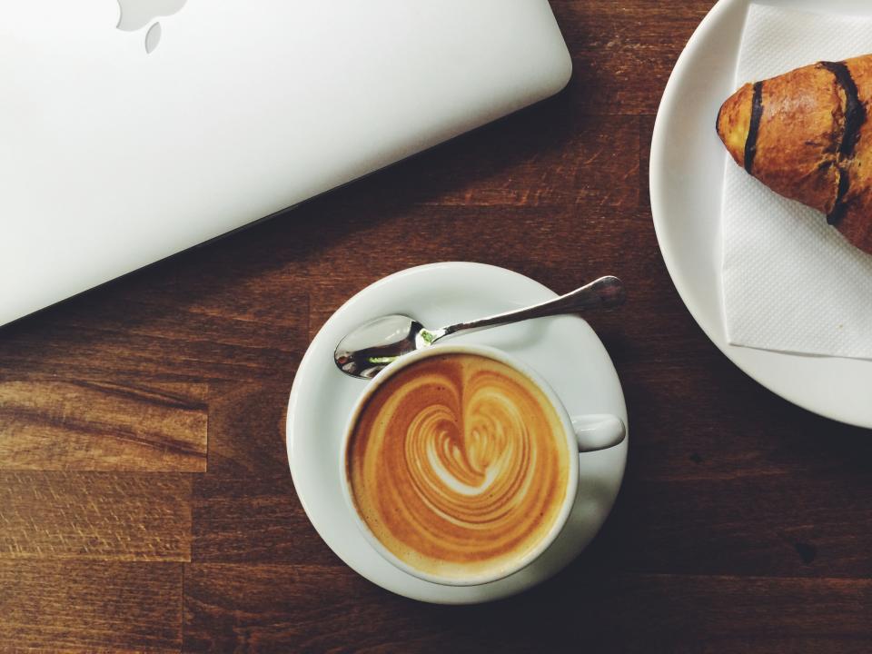 A latte beside a fresh croissant on a wooden table